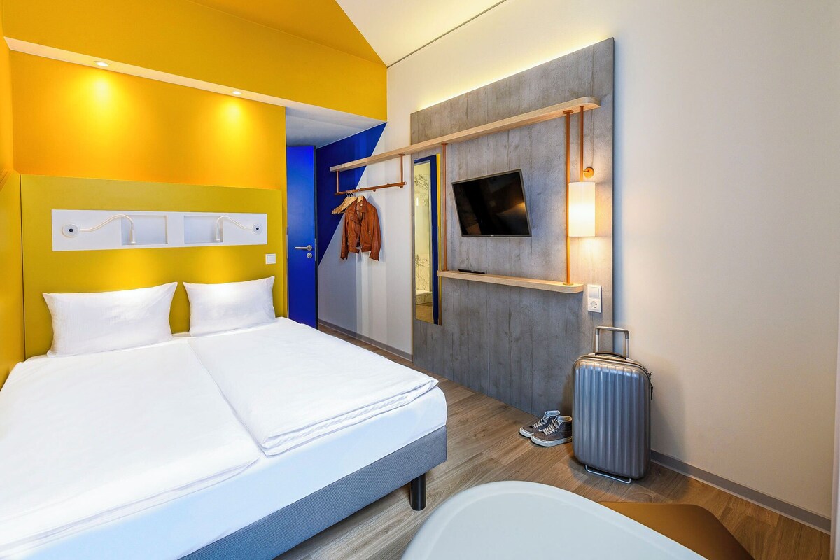 Een hotelkamer met een bed, een televisie, een spiegel en een koffer.