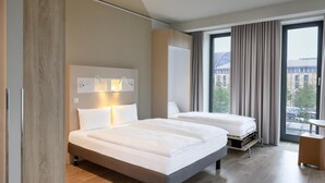 Una habitación de hotel moderna con dos camas, un ventanal con cortinas, suelo de madera y una mesita.