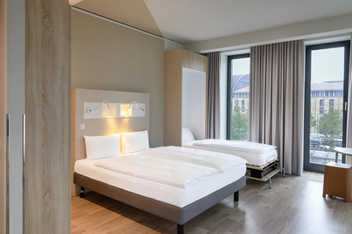 Een moderne hotelkamer met twee bedden, een groot raam met gordijnen, een houten vloer en een kleine tafel.