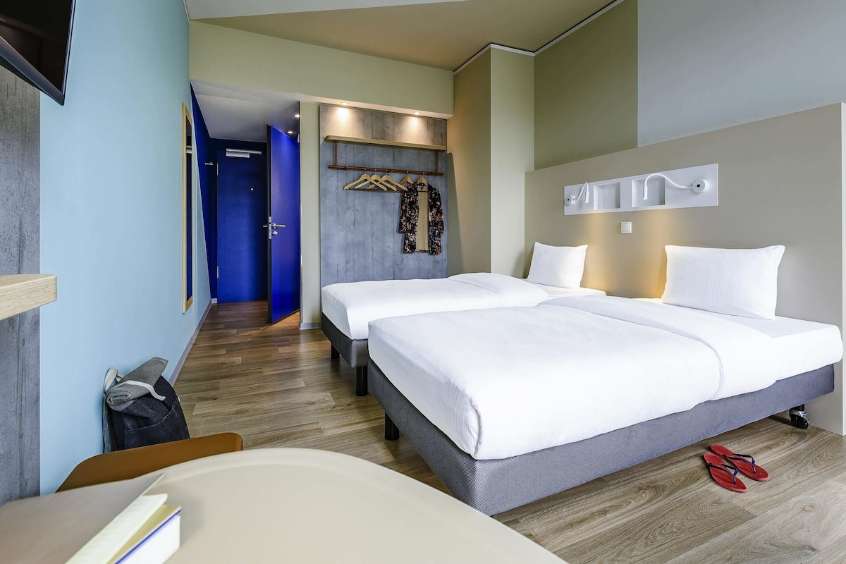 Une chambre d’hôtel avec deux lits, un bureau, une chaise, une télévision et une armoire.