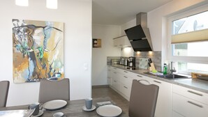 A modern kitchen with white cabinets, a black range hood, and a window with blinds. - Villa Paradiso, outdoor whirlpool and sauna for exclusive use, 100m to the lake (Göhren-Lebbin)