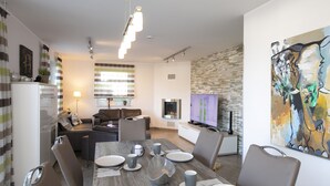 A modern living room with a fireplace, a dining area with a wooden table and chairs, and a living area with a sofa and TV. - Villa Paradiso, outdoor whirlpool and sauna for exclusive use, 100m to the lake (Göhren-Lebbin)