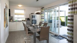A modern kitchen with a dining area, featuring a large table, chairs, and a sliding glass door leading to a patio. - Villa Paradiso, outdoor whirlpool and sauna for exclusive use, 100m to the lake (Göhren-Lebbin)