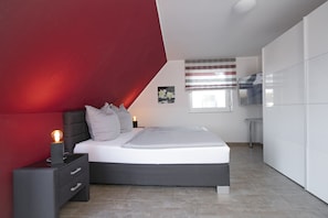 Quarto moderno com cama, mesa de cabeceira e uma parede de destaque vermelha.