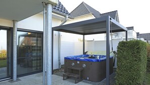 An outdoor hot tub area with a covered seating area, a wooden bench, and a hedge. - Villa Paradiso, outdoor whirlpool and sauna for exclusive use, 100m to the lake (Göhren-Lebbin)