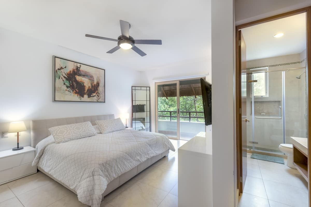 Un dormitorio moderno con una cama grande, un ventilador de techo, un cuadro y vistas a un balcón y zona de ducha.