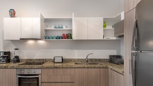A modern kitchen with white cabinets, a granite countertop, a built-in oven, a sink, and a stainless steel refrigerator. - Paramar Terra by Tulumeando (Tulum)