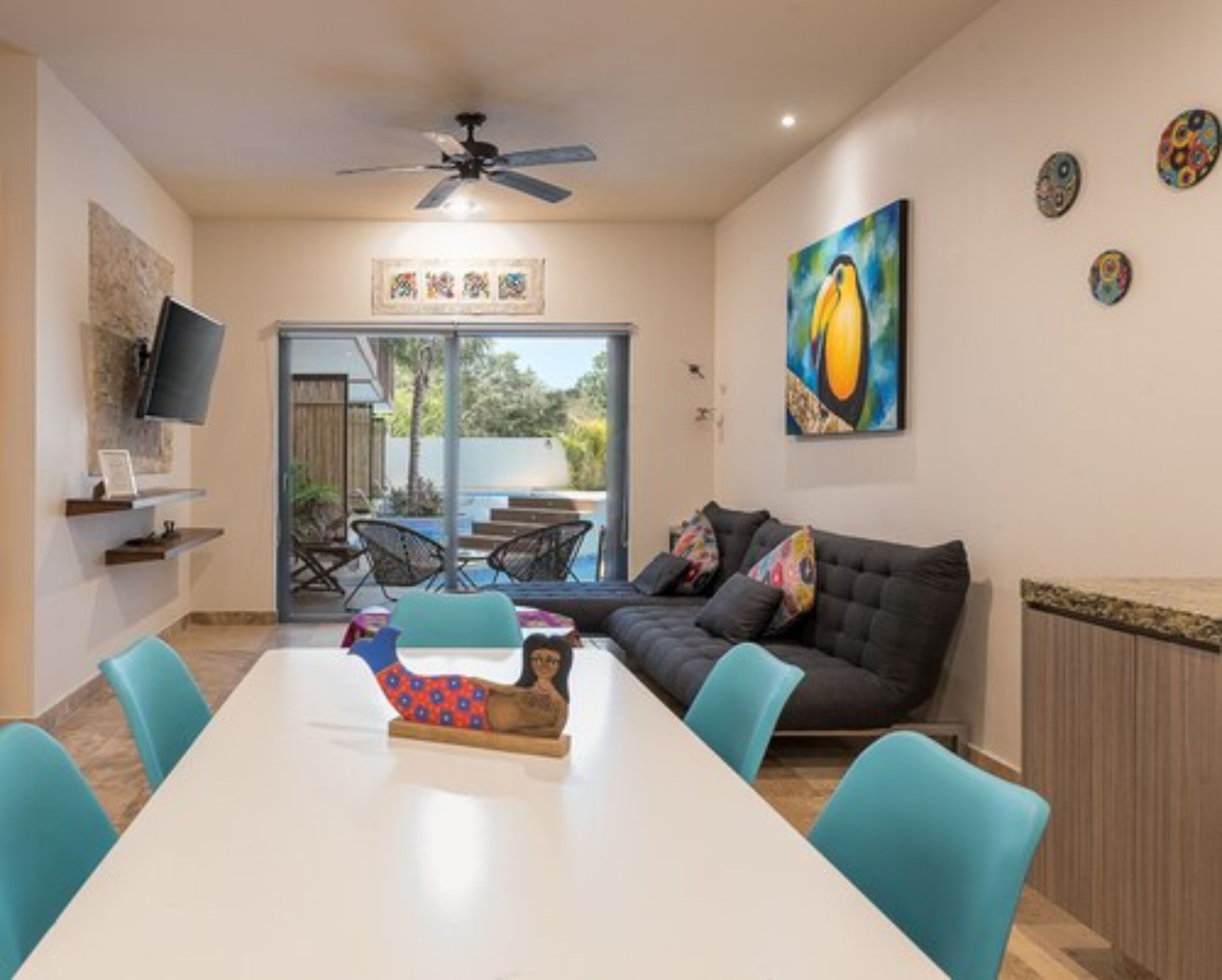 Un salon moderne avec un canapé, une table à manger et des chaises, un ventilateur de plafond et des œuvres d’art accrochées aux murs.