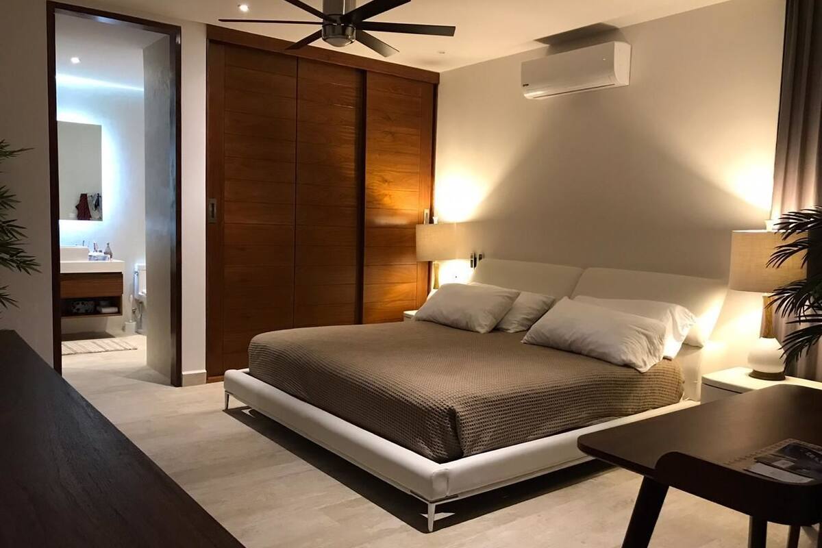 A modern bedroom with a bed, bedside tables, a ceiling fan, and a wardrobe.