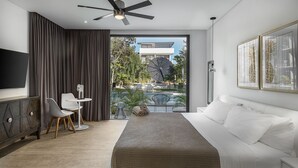 Una habitación de hotel moderna con una cama grande, un ventilador de techo, un área de comedor con una mesa y sillas, y vistas al exterior.