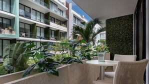A modern hotel balcony with wicker furniture, lush greenery, and a view of adjacent buildings.