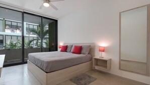A modern bedroom with a large bed, two bedside lamps, a ceiling fan, and a view of greenery outside.