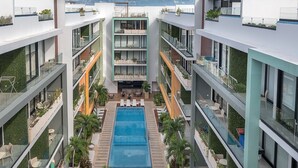 A modern hotel with a central pool, multiple balconies, and outdoor seating areas.