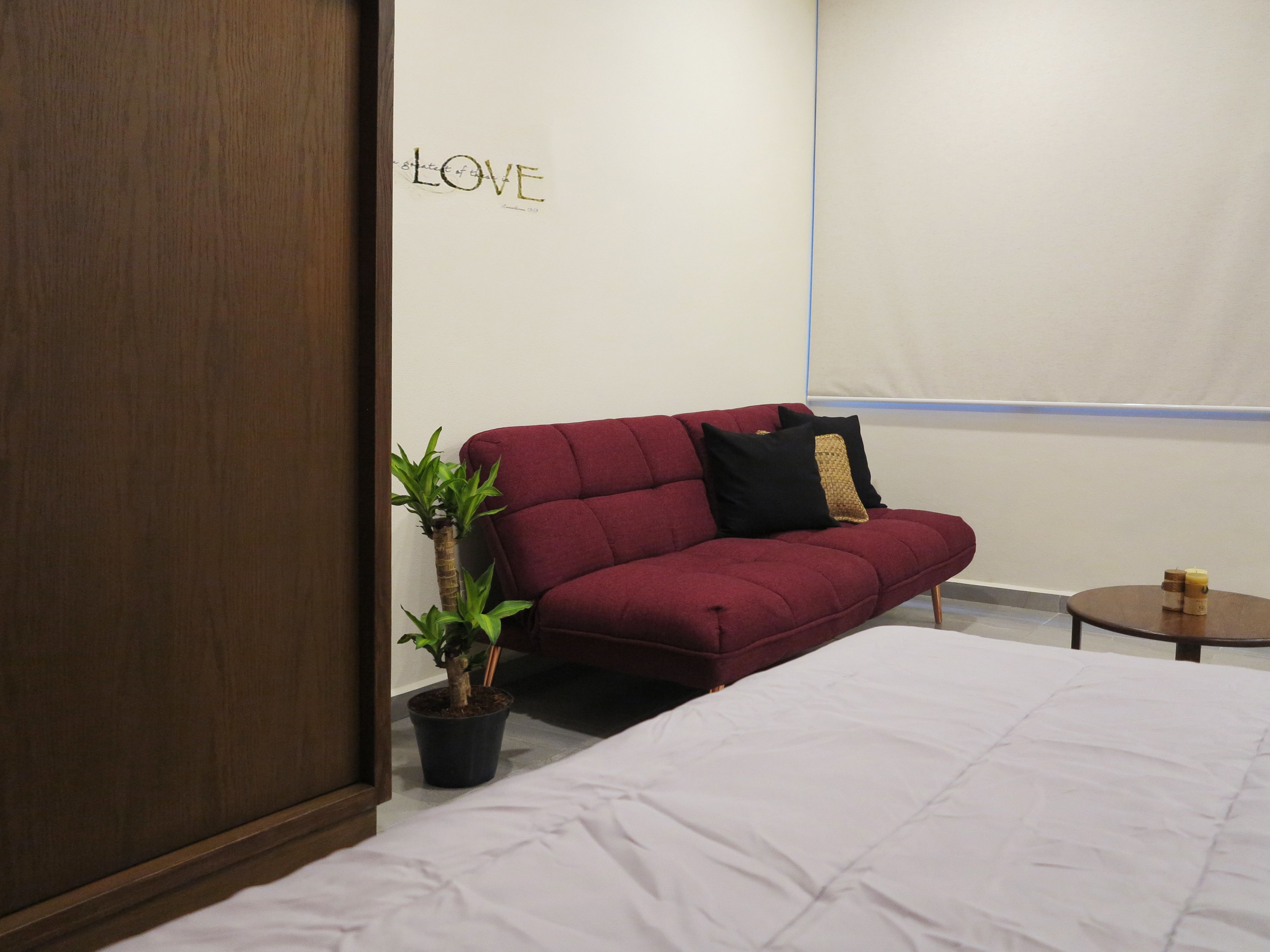 A hotel room with a red sofa, a small table with candles, a potted plant, and a bed with white bedding.