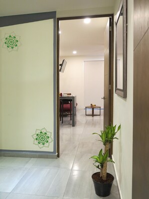 Un couloir avec une plante en pot, un bureau avec une chaise et un lit à l’arrière-plan.