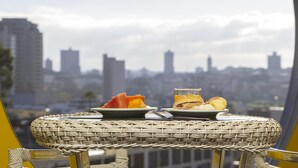 A wicker table with breakfast items and a glass of orange juice, overlooking a city skyline. - JP Palace Hotel (Franca)
