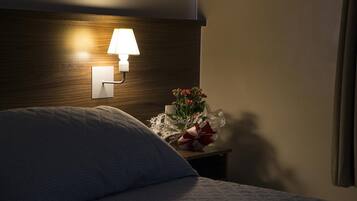 Una cama bien hecha con una almohada, una lámpara de noche y una mesita con un florero y un regalo envuelto.