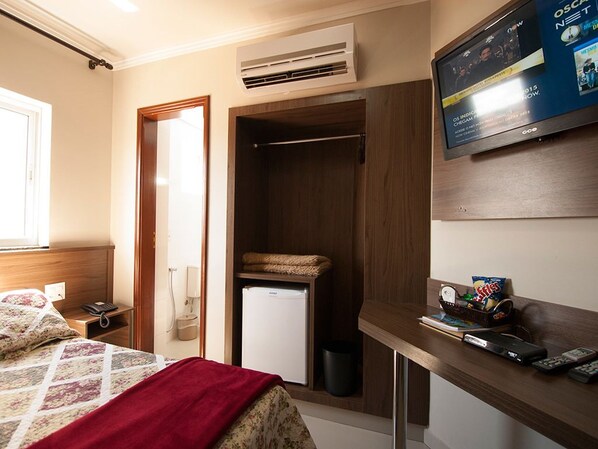 Una habitación de hotel compacta con cama, un escritorio pequeño con televisor, un refrigerador y un armario.