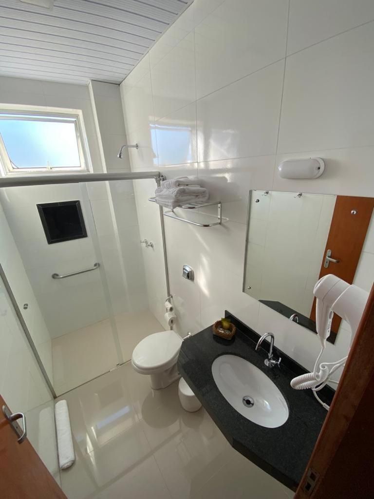 Un baño moderno con ducha envuelta en vidrio, inodoro blanco, lavamanos con espejo y un perchero para toallas.