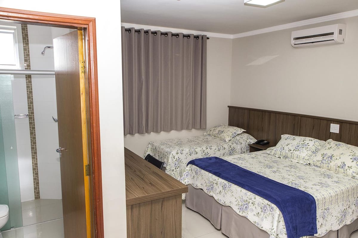 Een slaapkamer met twee bedden, een houten bureau, een badkamer met douche en een airconditioning.
