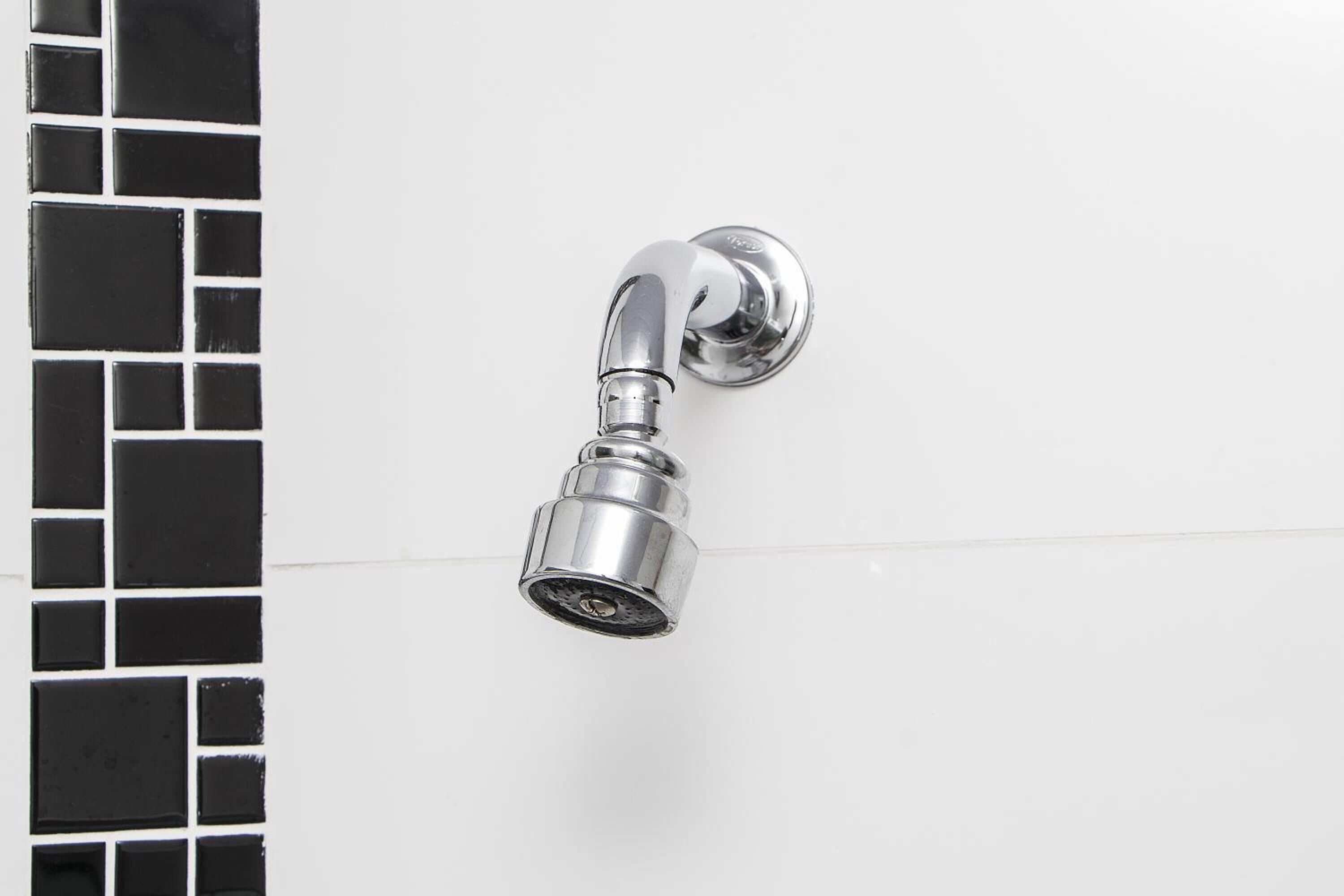 Un cabezal de ducha cromado sobre una pared blanca con un diseño de azulejos negros.