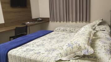 A bedroom with a bed, a desk, and a television on the wall.