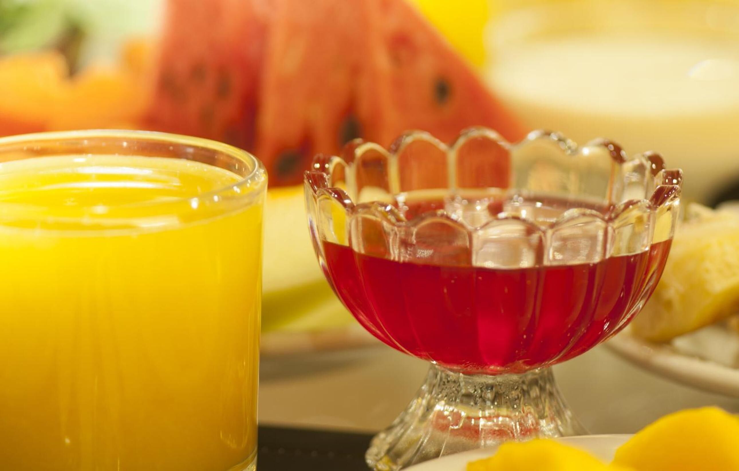 A glass of orange juice and a glass of red liquid in a decorative bowl.