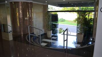 A modern hotel lobby with a glass entrance, a staircase, and potted plants.