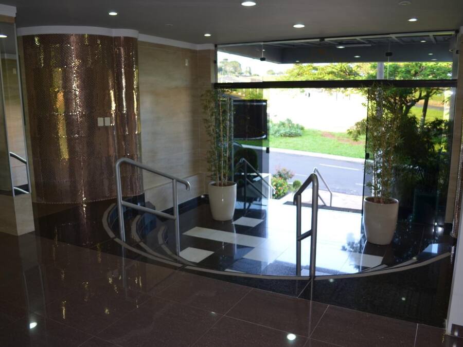 A modern hotel lobby with a glass entrance, a staircase, and potted plants.