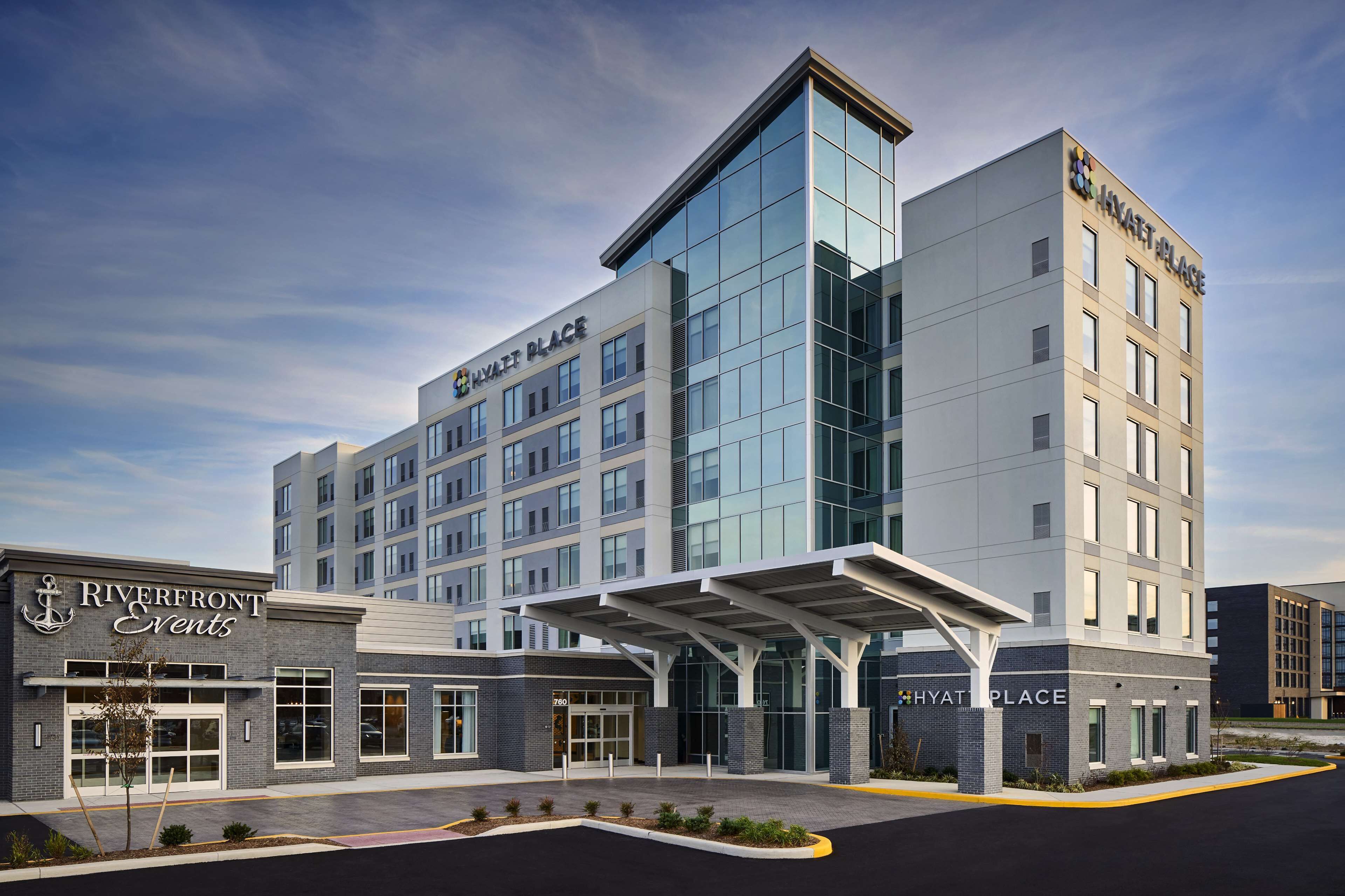A modern hotel with a glass facade, a covered entrance, and signage for 'Riverfront Events' and 'Hyatt Place'.