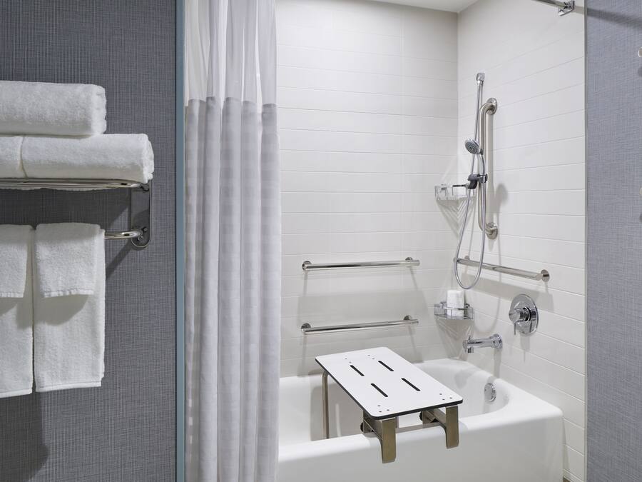A modern bathroom with a bathtub, shower, and handrails. There are towels on a rack and a shower curtain.