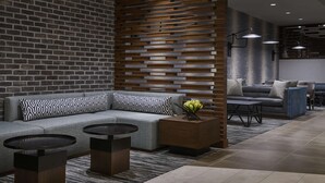A modern interior with a brick wall, wooden slats, a grey sofa, two round tables, and a blue accent wall. - Hyatt Place Wilmington Riverfront (Wilmington)