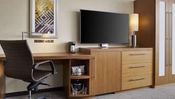 A hotel room with a wooden desk, a television, a lamp, a chair, and a cabinet with drawers.