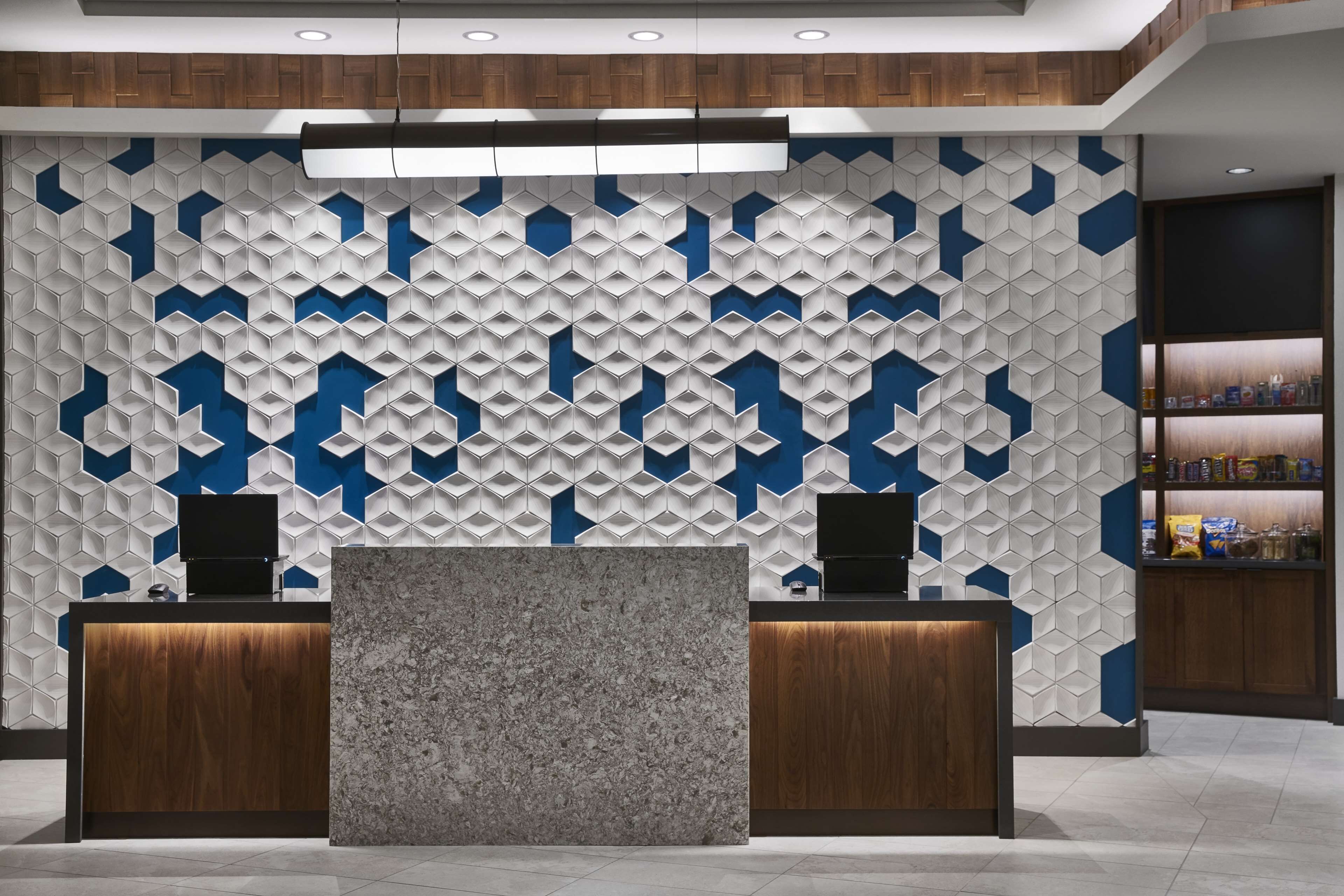 Zona de recepción con una pared de diseño geométrico, dos mostradores de madera y una estantería con objetos a la derecha.