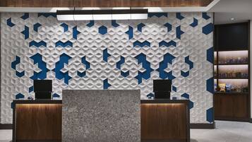 Zona de recepción con una pared de diseño geométrico, dos mostradores de madera y una estantería con objetos a la derecha.