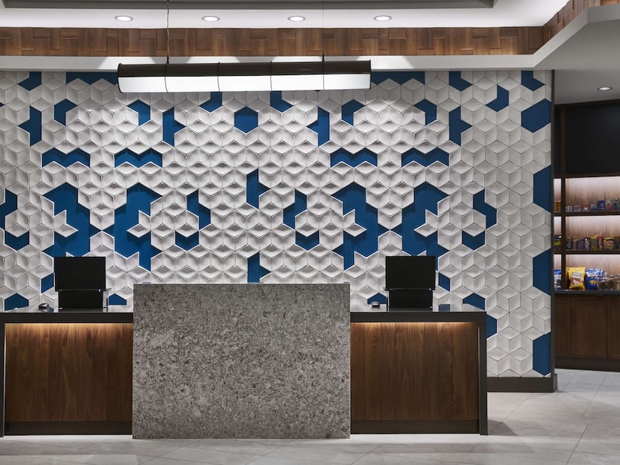 Zona de recepción con una pared de diseño geométrico, dos mostradores de madera y una estantería con objetos a la derecha.