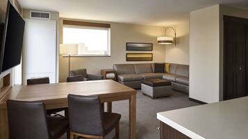 A hotel room with a dining table, chairs, a sofa, a TV, and a lamp.