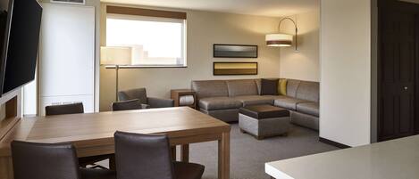 Habitación de hotel con una mesa de comedor, sillas, un sofá, un televisor y una lámpara.
