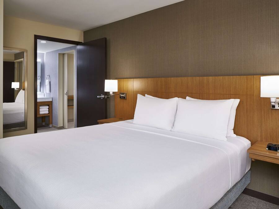 Ein Hotelzimmer mit einem großen Bett, einem Holzkopfstück, zwei Nachttischen mit Lampen und einer Tür zu einem Badezimmer.