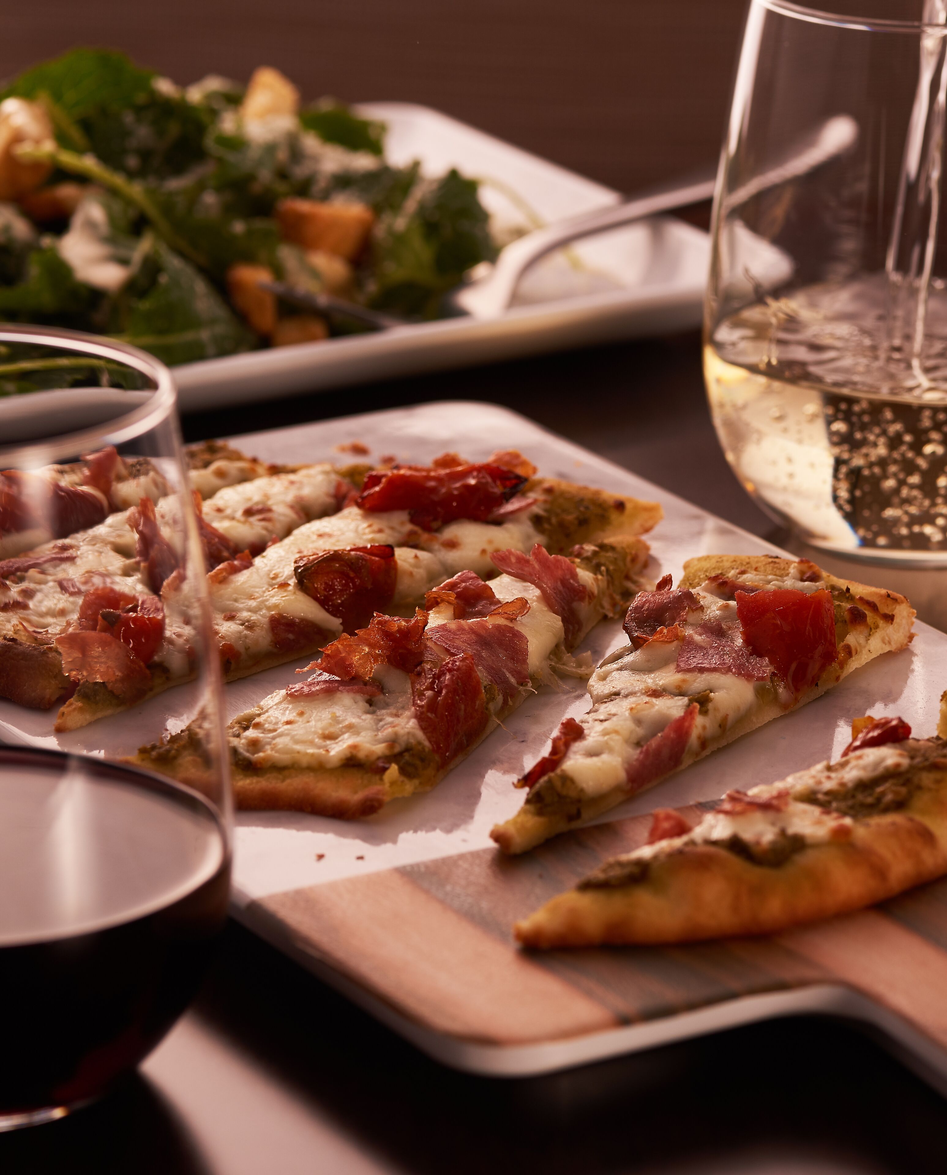 Uma mesa com fatias de pizza, um copo de vinho branco e uma salada.