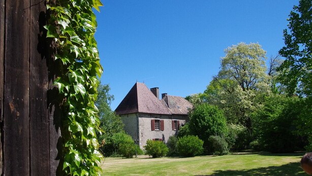 A stone building with a steep roof, surrounded by a well-maintained lawn and trees.