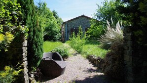 A rustic stone building with a red roof, surrounded by lush greenery and a gravel path leading to it.