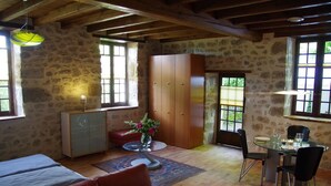 A rustic room with stone walls, a wooden ceiling, a dining table with chairs, a sofa, and a cabinet.