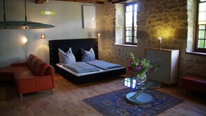 A bedroom with a bed, a sofa, a table with a vase, and a window with curtains.