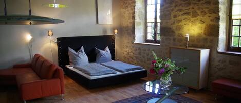 Une chambre à coucher avec un lit, un canapé, une table avec un vase et une fenêtre avec des rideaux.