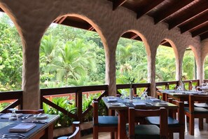 A restaurant with outdoor seating, wooden tables, and chairs, surrounded by lush greenery. - Tabacon Thermal Resort AND SPA (La Fortuna)
