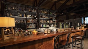 A bar area with wooden shelves stocked with liquor bottles, a wooden bar counter, and bar stools. - Tabacon Thermal Resort AND SPA (La Fortuna)