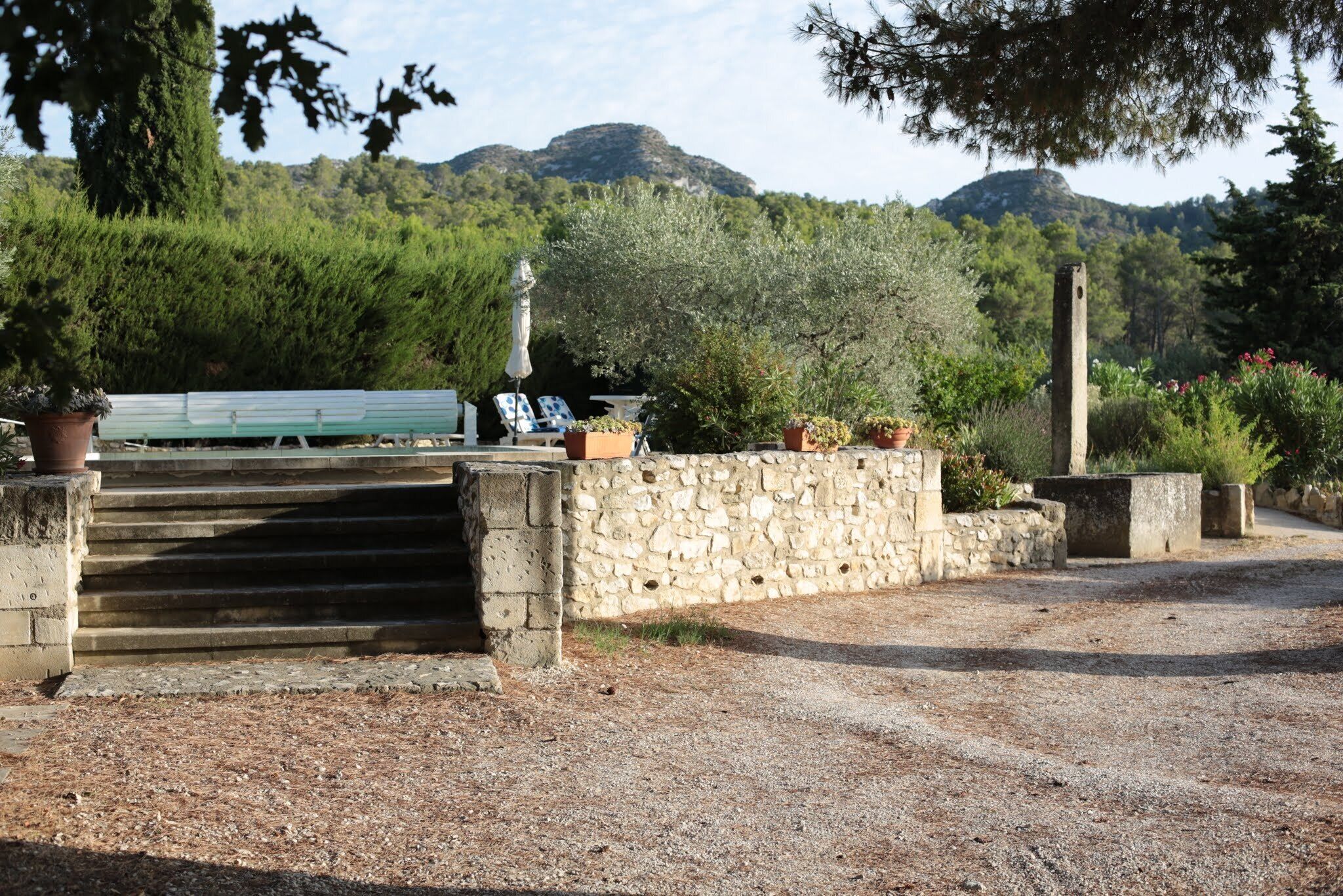 A stone staircase leading to a seating area with a bench and potted plants, surrounded by a gravel path and greenery.