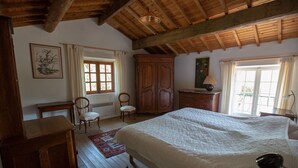 A spacious bedroom with a large bed, wooden furniture, and a view of the outdoors through a window. - Authentic farmhouse in Saint Remy de Provence (Saint-Rémy-de-Provence)