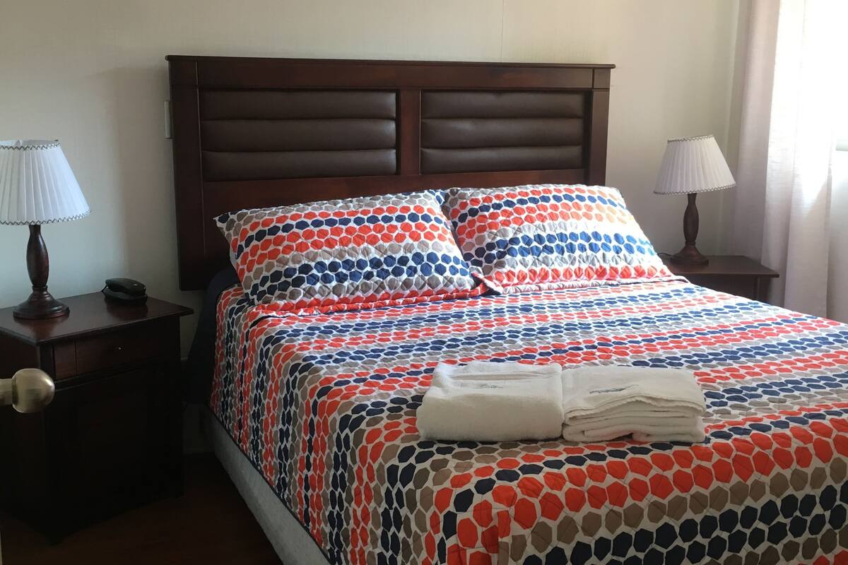 A neatly made bed with a patterned bedspread, two bedside tables with lamps, and a wooden headboard.